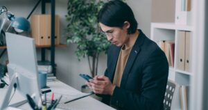 Jovem em um escritório usando smartphone enquanto trabalha em uma mesa de computador